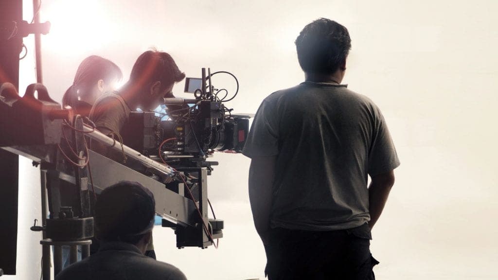 A real behind-the-scenes photograph of a film crew working around a professional camera on set, standing in for a directable video production workflow.