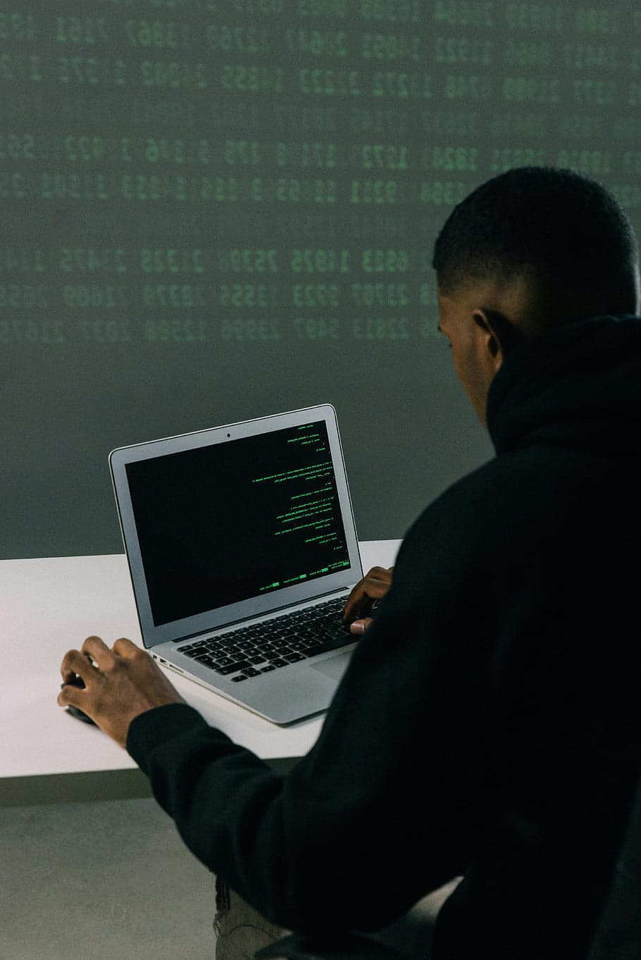 A developer in a hoodie working on a MacBook showing code on screen in a dark room