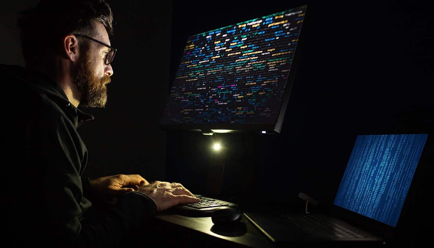 A real photograph of a man looking at colorful code on a large screen at night; it is not a screenshot of the Gemini product interface.