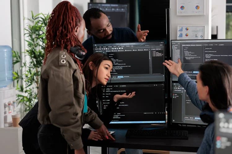 Software development team collaborating around computer screens reviewing code in an office