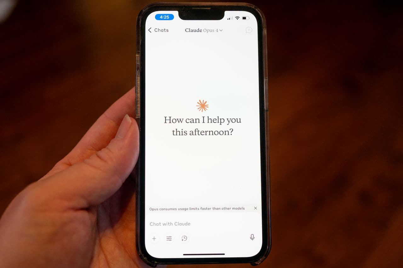 手机上的 Claude 应用界面:用户手持 iPhone,屏幕显示 Claude 对话入口