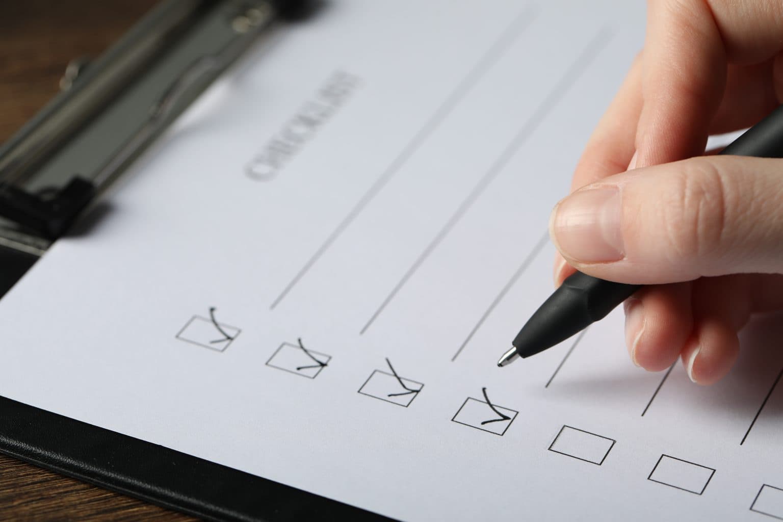 A real photograph of a hand ticking items on a task checklist with a pen, standing in for task acceptance and item-by-item verification.