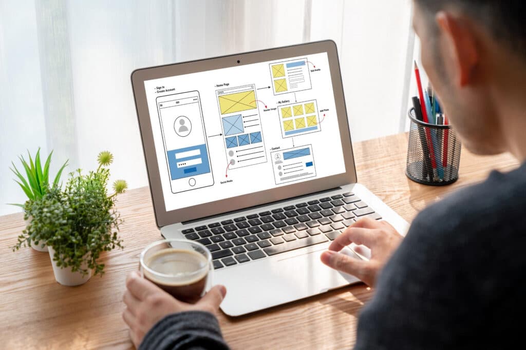 A beginner learning at a laptop with website wireframes: non-programmers can ship their first webpage with AI