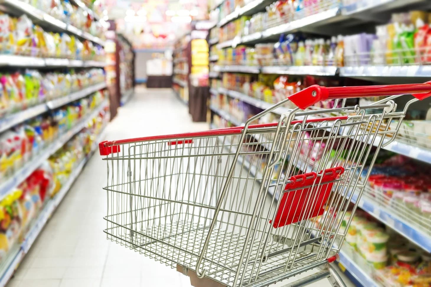 A real photograph of a shopping cart full of groceries in front of supermarket shelves, standing in for agent-assisted shopping.