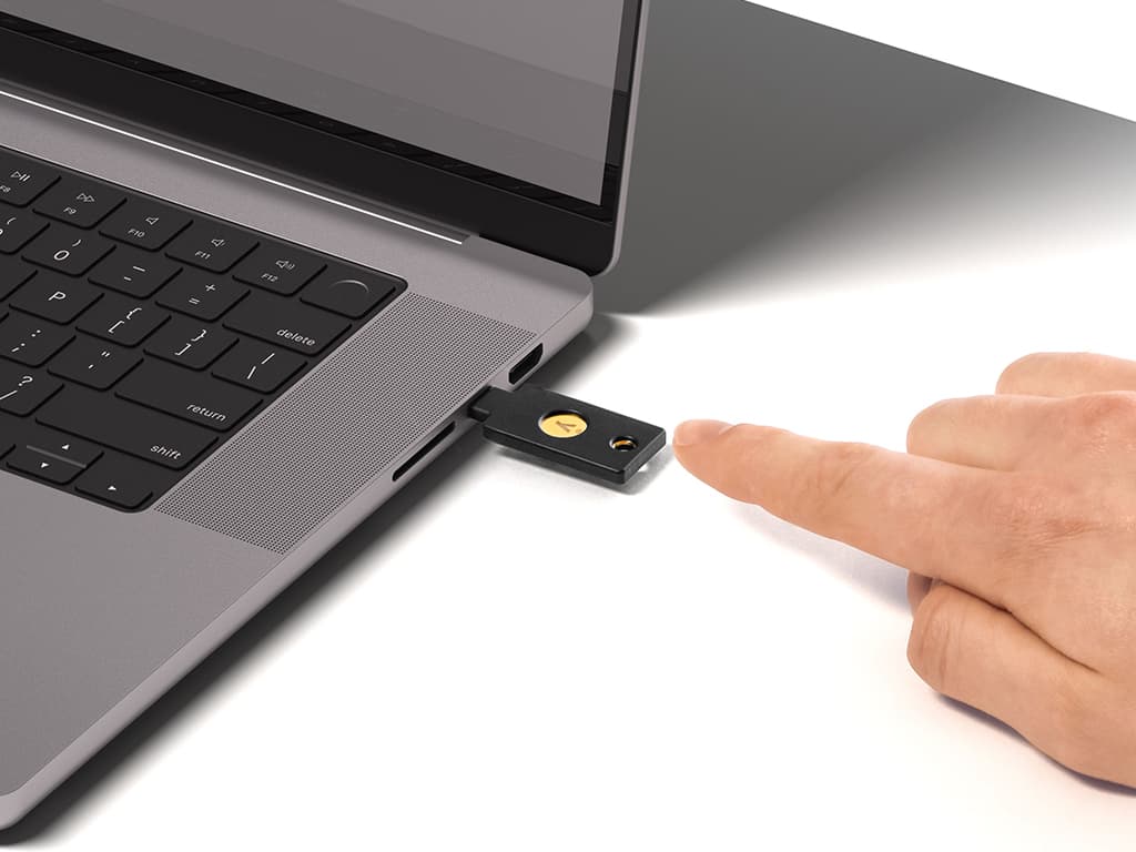 A finger touching a hardware security key plugged into a laptop