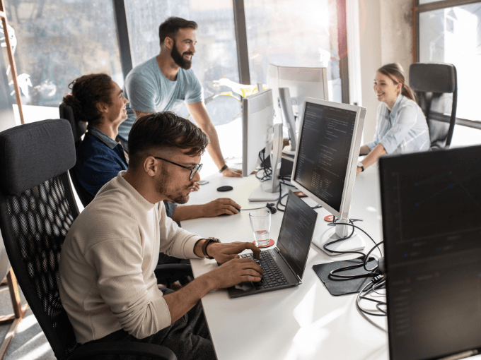 A real photograph of developers collaborating around computers in an office; it is not a screenshot of GitHub.