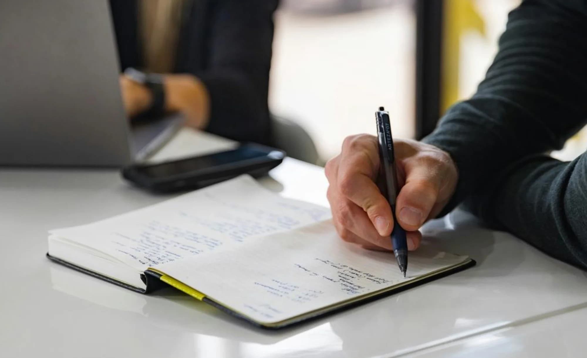 A real photograph of someone writing notes at a desk, standing in for the work of writing release notes.