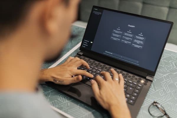 Over-the-shoulder photo of a person typing to an AI chat assistant on a laptop, with the conversation interface visible on screen