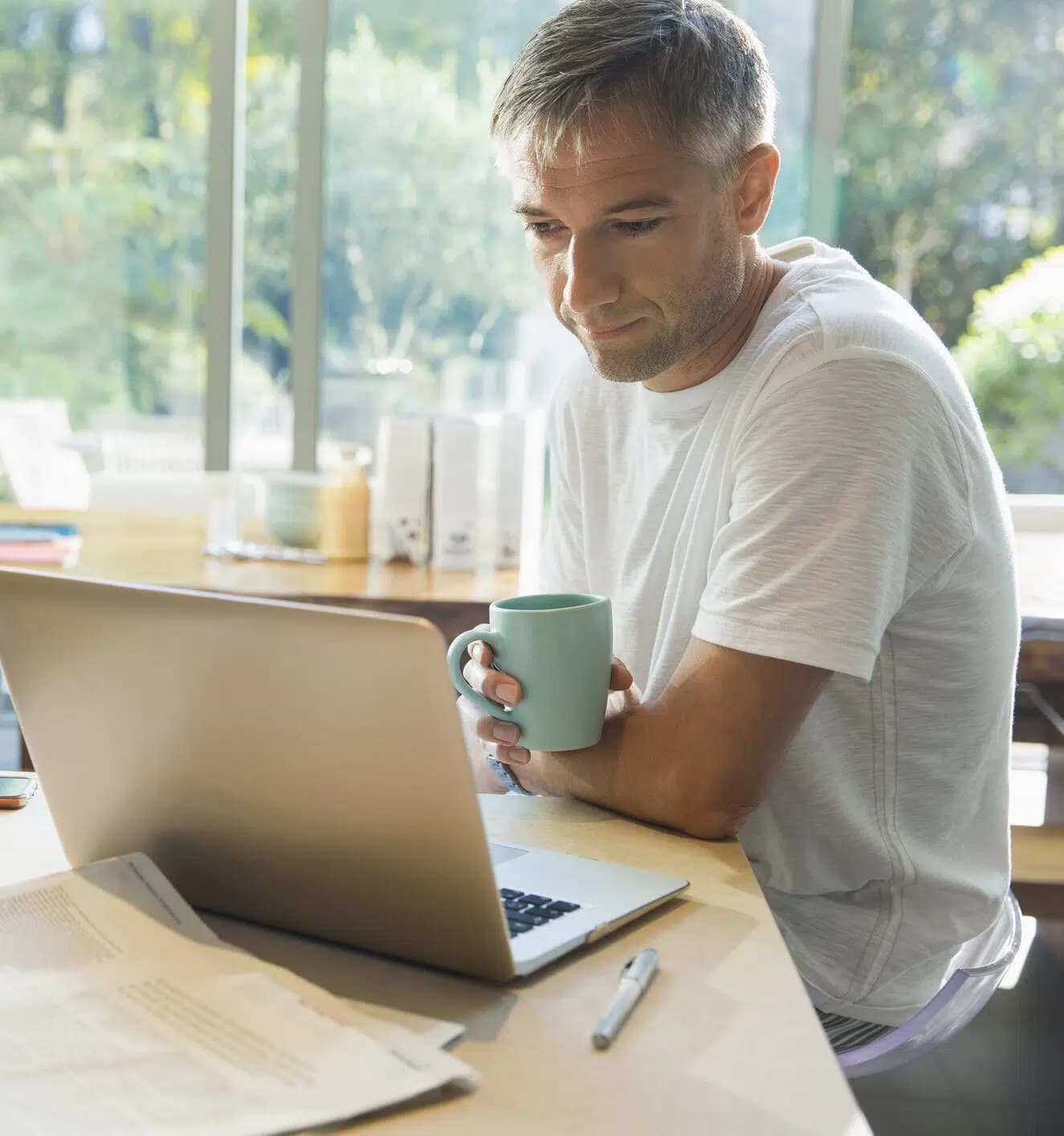 A real photograph of a man holding a coffee mug and reading at a laptop; it is not a screenshot of any product interface discussed in the article.