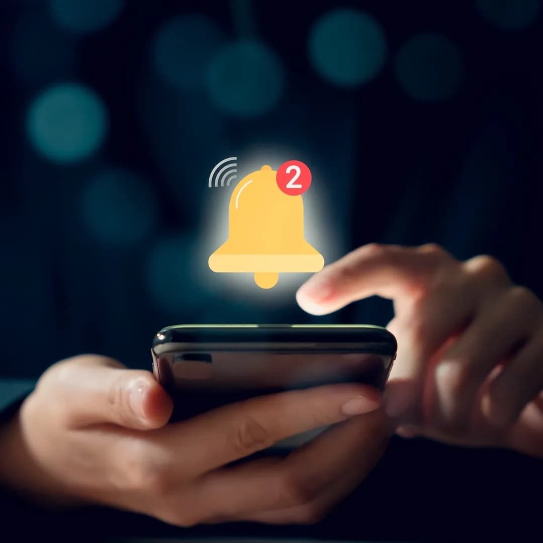 A real photograph of hands holding a phone with a notification bell graphic overlaid; it is not a screenshot of a system permission dialog.