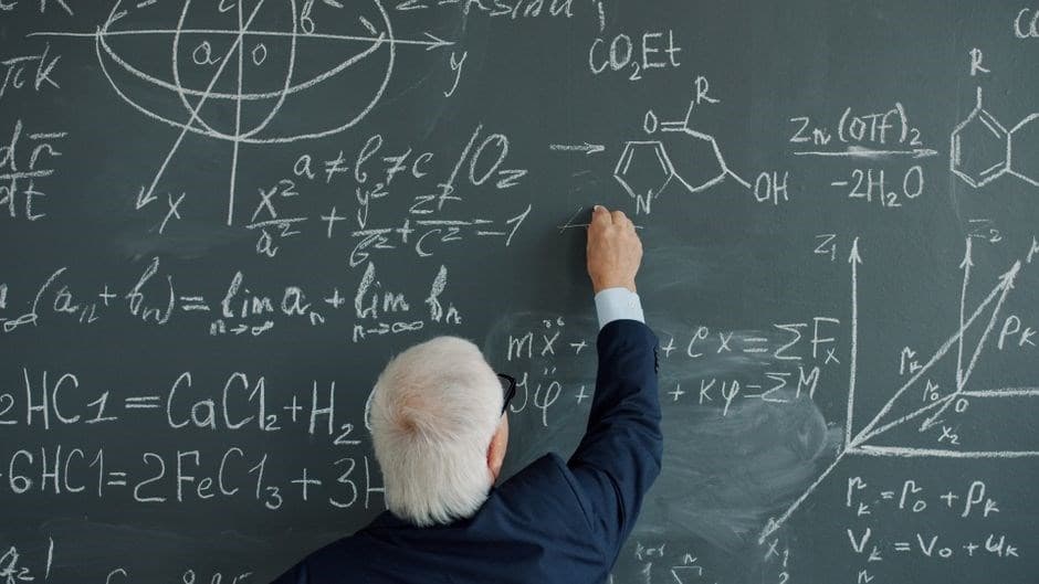 A white-haired professor, seen from behind, writing on a chalkboard covered with mathematical formulas and geometric diagrams.