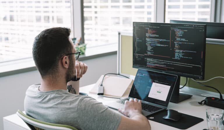 A real photograph of a developer working at a screen full of code, not a screenshot of Visual Studio or any Microsoft product interface
