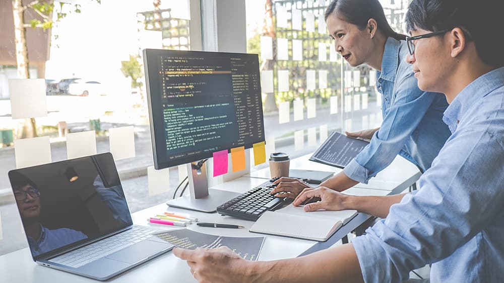 Two developers reviewing code on monitors in an office, illustrating the Claude API 2026-10-21 migration guide