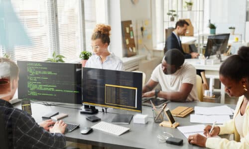 A real photograph of developers working at computer screens in an office; it is not a screenshot of GitHub or Copilot.