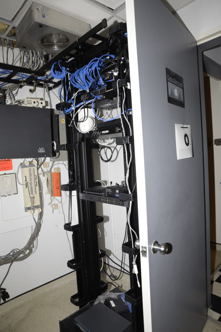 A real photograph of a server room filled with networking equipment cables and rack-mounted servers.