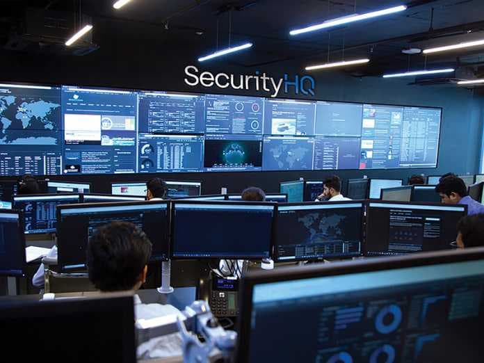 A real photograph of staff working at monitoring screens in a SecurityHQ security operations center; it is not a screenshot of Anthropic's product interface.
