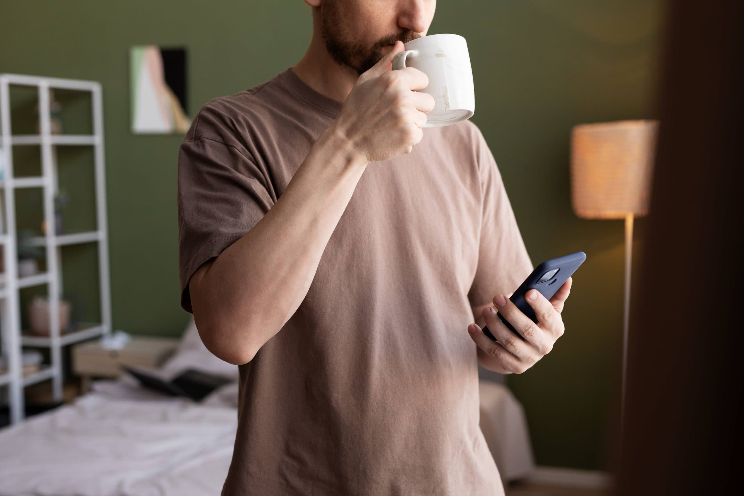 A man drinking coffee while checking his phone for a login email