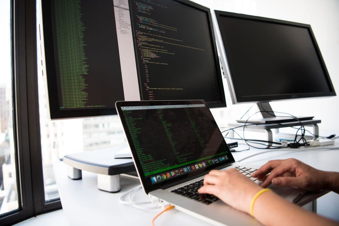 A developer typing code on a laptop in front of multiple monitors, illustrating a decision layer wired into production workflows