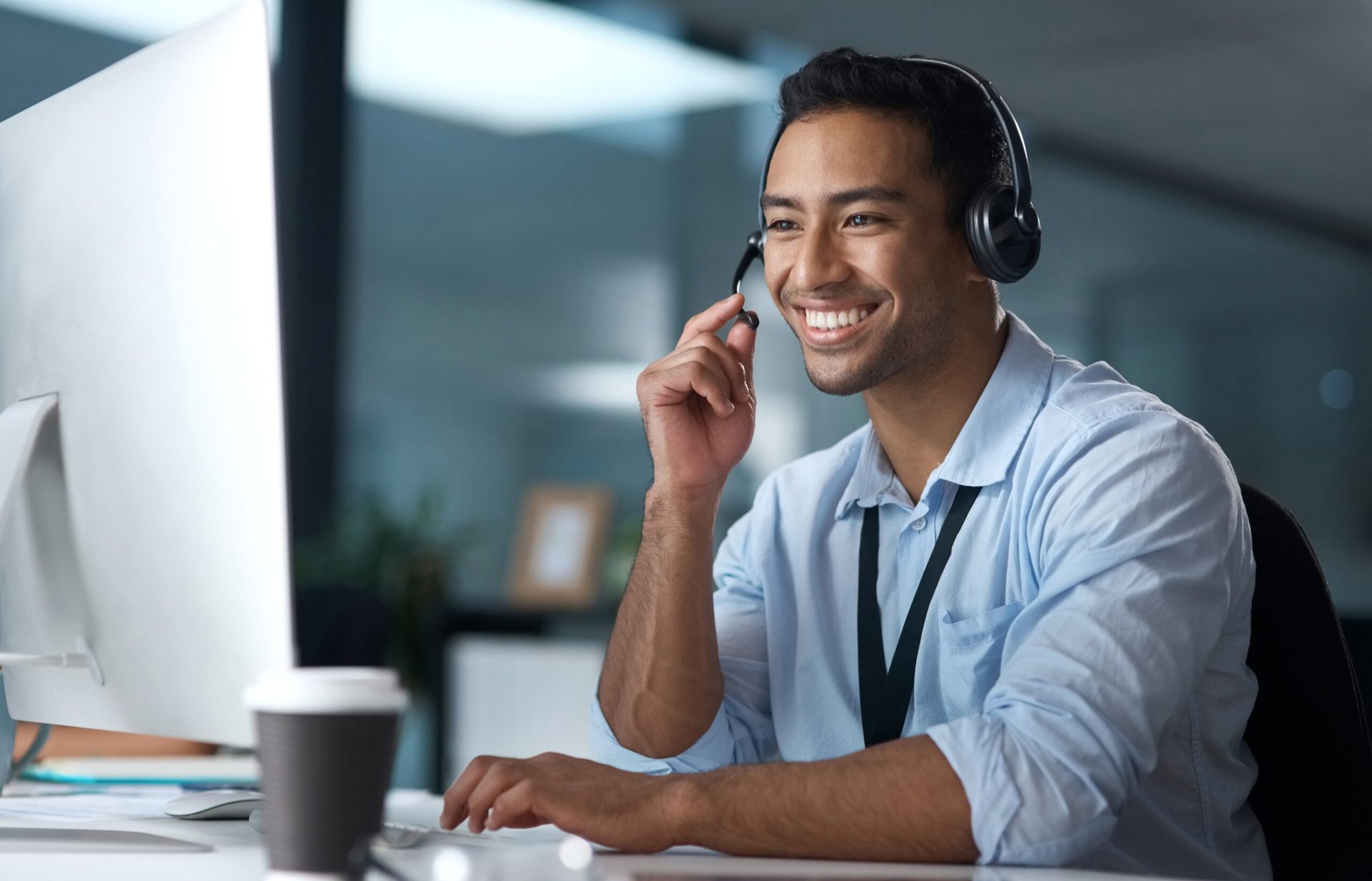 A customer service agent with a headset smiling at his monitor