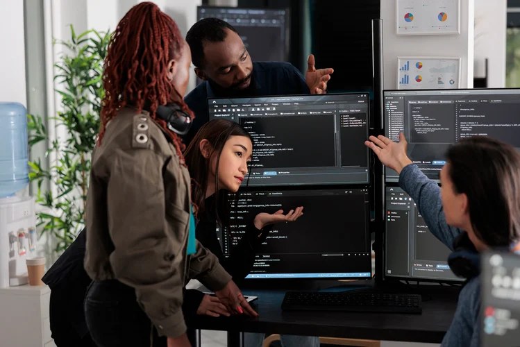 Software development team collaborating around computer screens reviewing code in an office