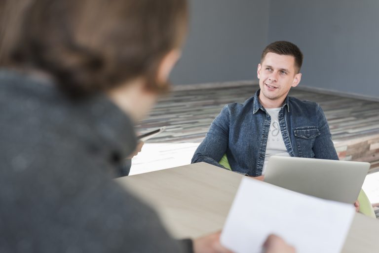 A job interview in progress: a young developer with a laptop faces the interviewer as competition for junior roles intensifies