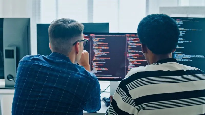 Two developers sitting side by side reviewing code on a monitor