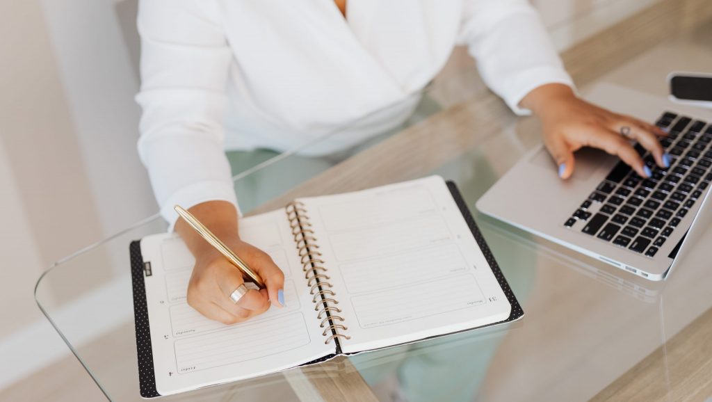 Writing-themed cover: person writing notes beside a laptop on a wooden desk